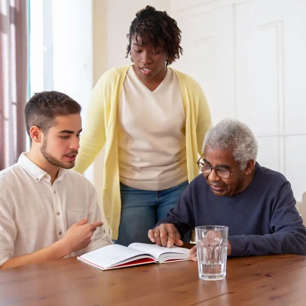 Deux jeunes adultes partagent un moment de lecture avec un homme âgé, autour d’une table (photo d’illustration)