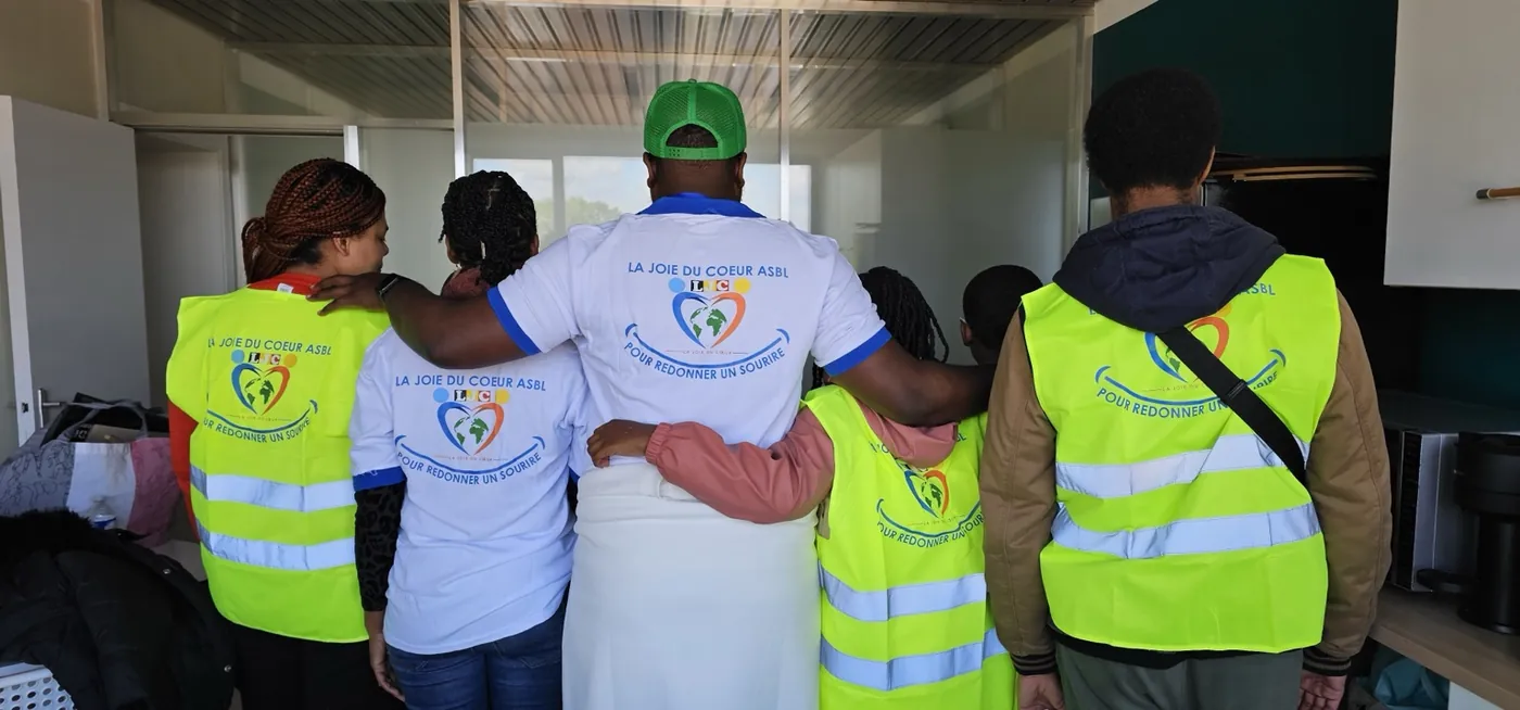 Bénévoles de La Joie du Cœur vus de dos, se tenant par les épaules, en gilets et t-shirts « Pour redonner un sourire »